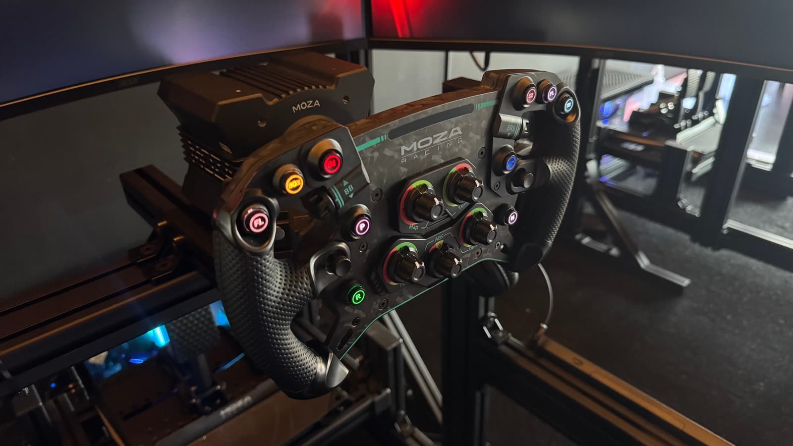 Close-up of the racing wheel with triple-monitor setup in the background